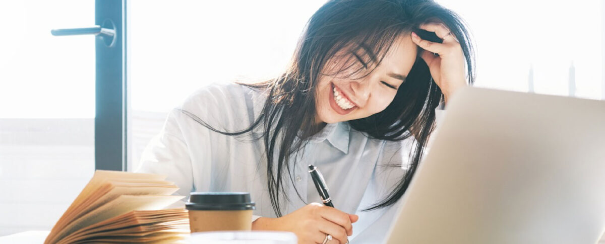 Student with long dark hair smiling while using a pen sitting at a table